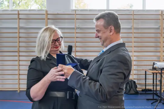 Wręczenie odznaczenia przez mężczyznę kobiecie w formalnym stroju.