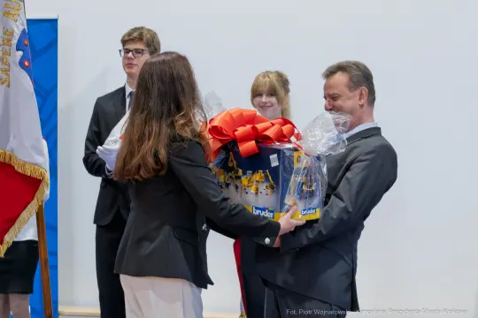 Wręczenie prezentu z dużą czerwoną kokardą podczas uroczystości.