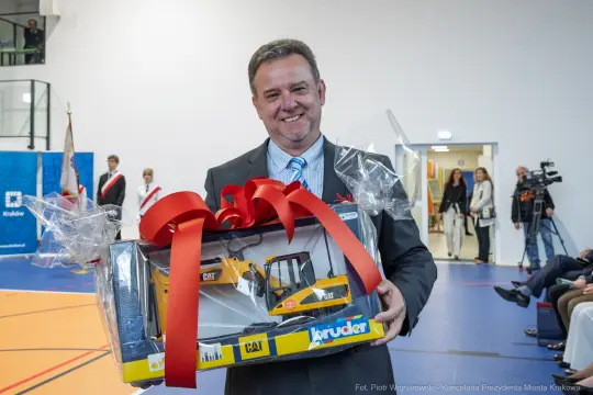 Mężczyzna trzyma model koparki z dużą czerwoną wstążką.