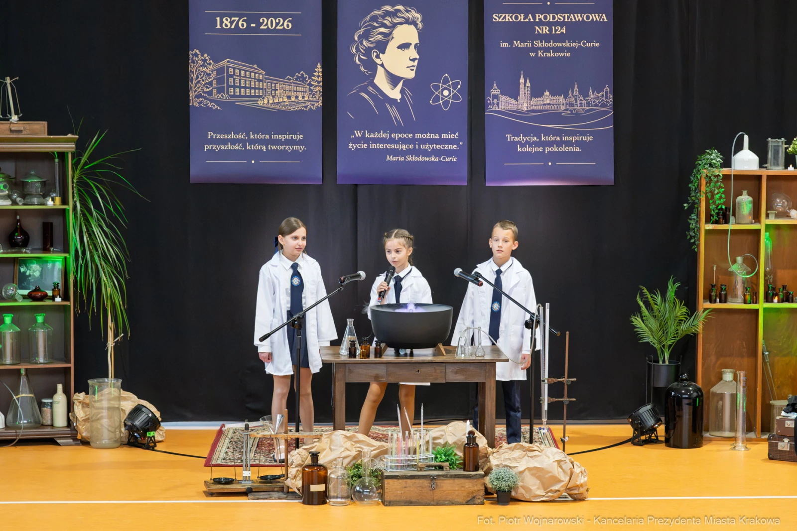 Uczniowie w białych fartuchach prezentują eksperymenty naukowe na scenie.  Autor: Piotr Wojnarowski