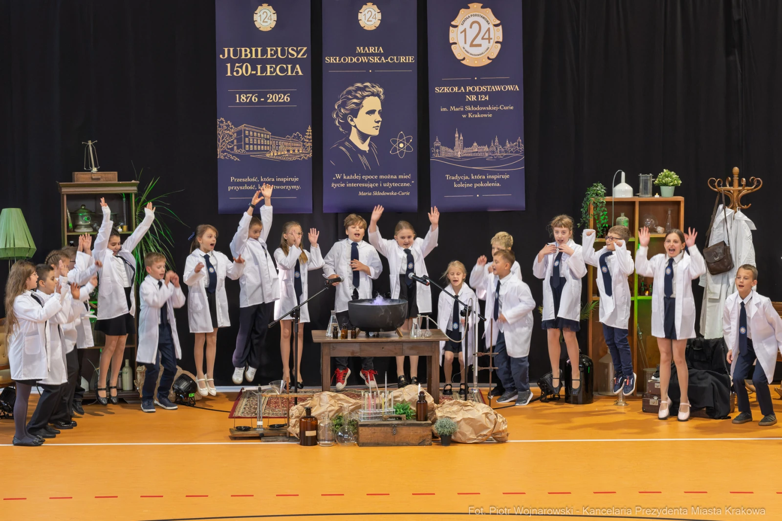 Uczniowie w białych fartuchach prezentują występ z okazji jubileuszu szkoły.  Autor: Piotr Wojnarowski