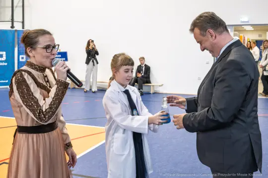 Dziecko wręcza butelkę wody dorosłemu mężczyźnie podczas wydarzenia.