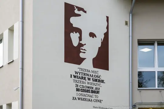 Portret z cytatem o wytrwałości i wierze w siebie na ścianie budynku.