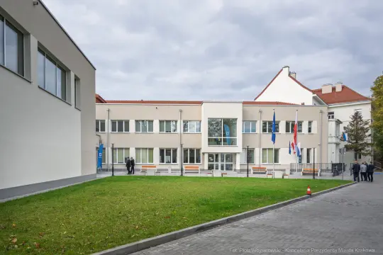 Budynek urzędowy z flagami, otoczony trawnikiem i chodnikiem.