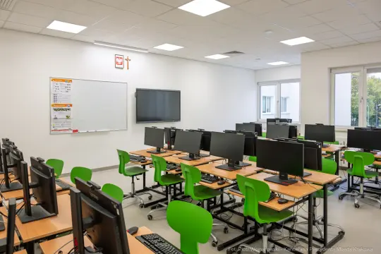 Pusty pokój komputerowy z zielonymi krzesłami i monitorami.