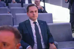 Mężczyzna w garniturze siedzący na widowni, z poważnym wyrazem twarzy.