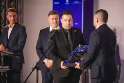 Mężczyzna w garniturze odbiera nagrodę podczas uroczystości wręczenia wyróżnień.