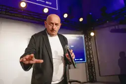 Mężczyzna z mikrofonem na scenie, gestykulujący w trakcie wystąpienia.