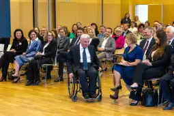 Grupa ludzi w sali konferencyjnej, wśród nich mężczyzna na wózku inwalidzkim.