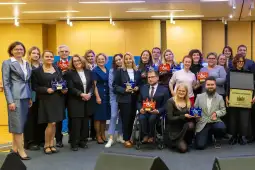 Grupa ludzi z nagrodami na tle sceny, uśmiechnięci, w formalnych strojach.