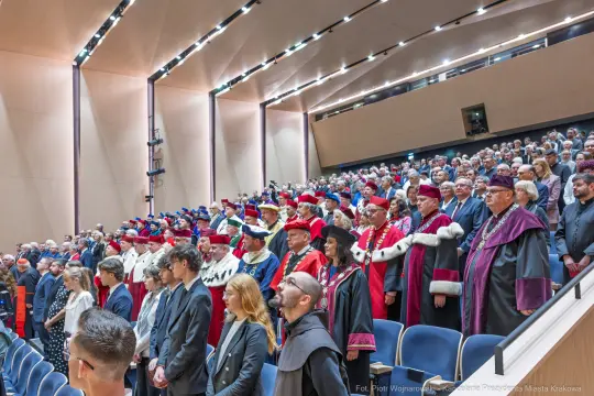 Uczestnicy ceremonii w strojach akademickich w sali wykładowej.