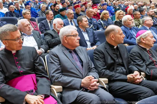 Grupa osób w formalnych strojach siedzących na widowni podczas wydarzenia.