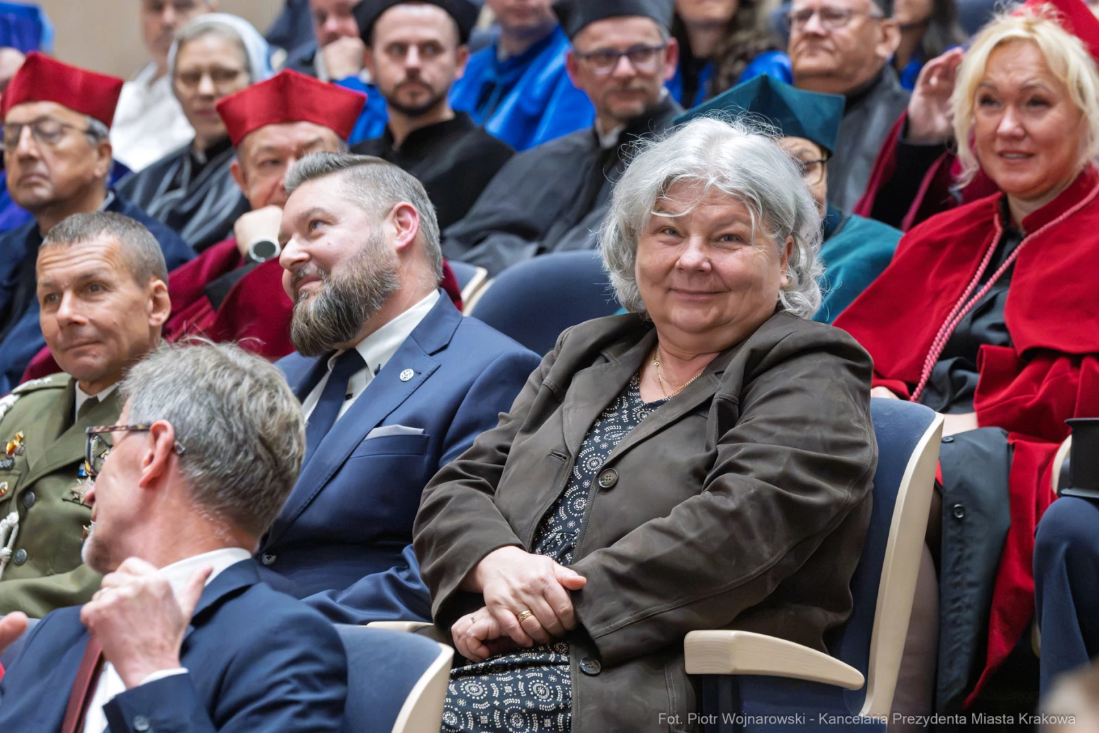Grupa osób w strojach akademickich i cywilnych, siedzących na widowni podczas uroczystości.  Autor: Piotr Wojnarowski