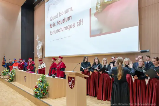 Uroczystość akademicka z chórem i przedstawicielami uczelni w togach.