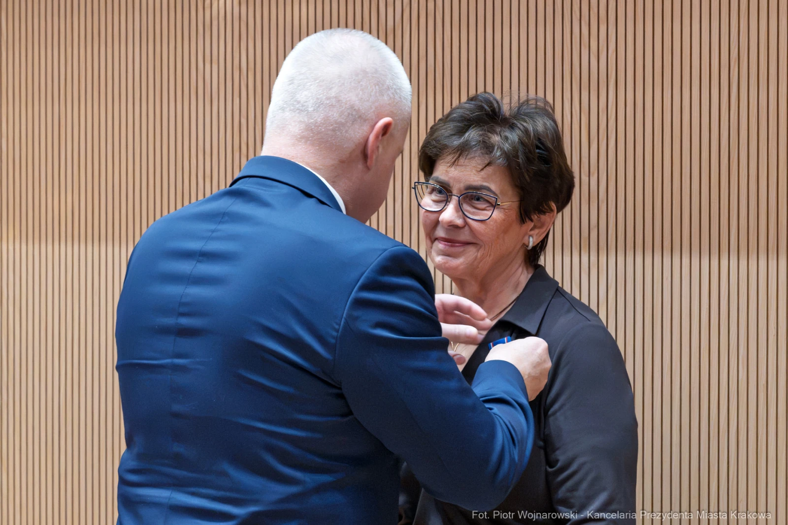 Wręczenie odznaczenia przez mężczyznę kobiecie w formalnym otoczeniu.  Autor: Piotr Wojnarowski