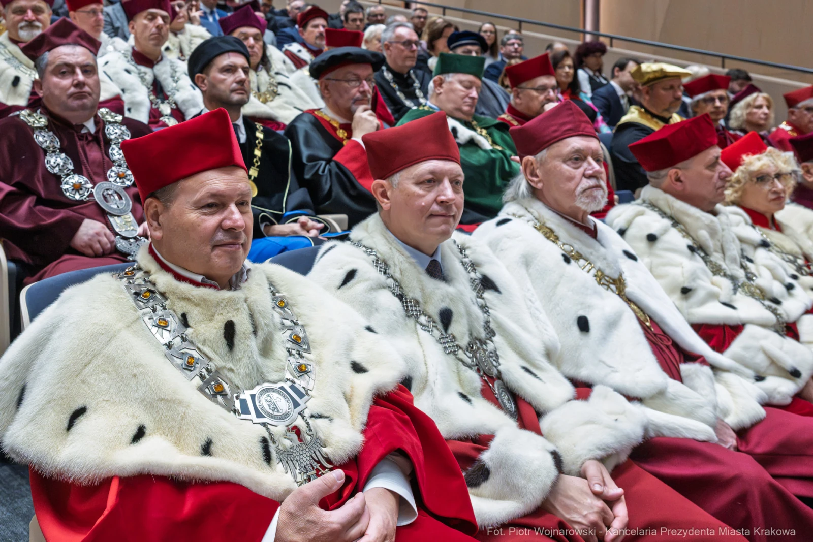 Grupa osób w tradycyjnych strojach z czerwonymi czapkami i łańcuchami, siedzących na uroczystości.  Autor: Piotr Wojnarowski