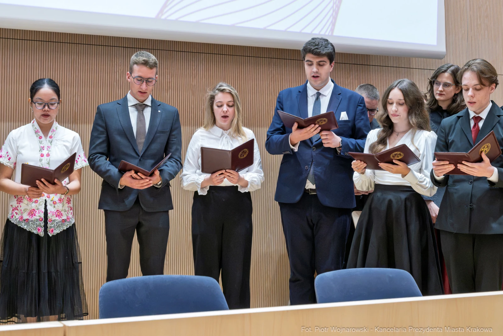 Grupa osób w eleganckich strojach śpiewa, trzymając dokumenty w rękach.  Autor: Piotr Wojnarowski