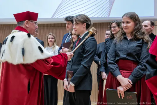 Ceremonia wręczenia dyplomów z udziałem rektora i absolwentów w akademickim otoczeniu.