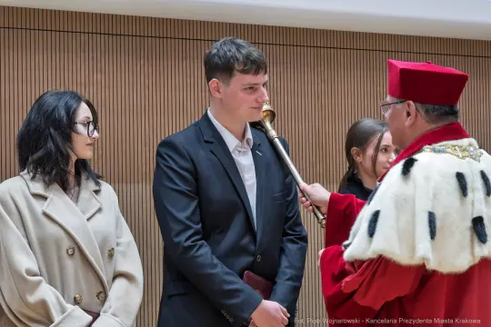 Ceremonia wręczenia nagrody, młody mężczyzna odbiera wyróżnienie od dostojnika w tradycyjnym stroju.