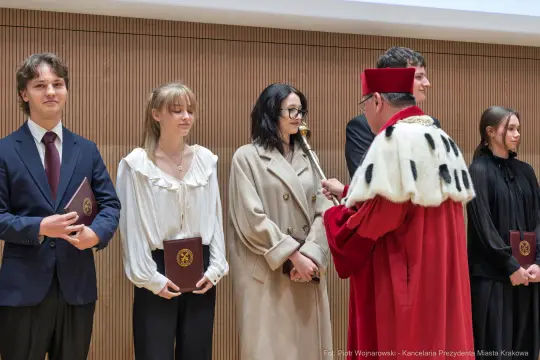 Uroczystość wręczenia dyplomów z udziałem studentów i przedstawiciela uczelni.