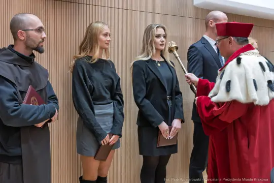 Ceremonia wręczenia dyplomów, uczestnicy w strojach formalnych.