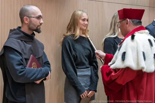 Ceremonia wręczenia nagród, mężczyzna w habicie i kobieta w eleganckim stroju.