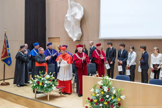 Uroczystość akademicka z uczestnikami w togach i strojach ceremonialnych.