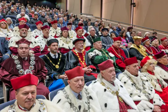 Uroczystość akademicka z uczestnikami w tradycyjnych strojach i czapkach.