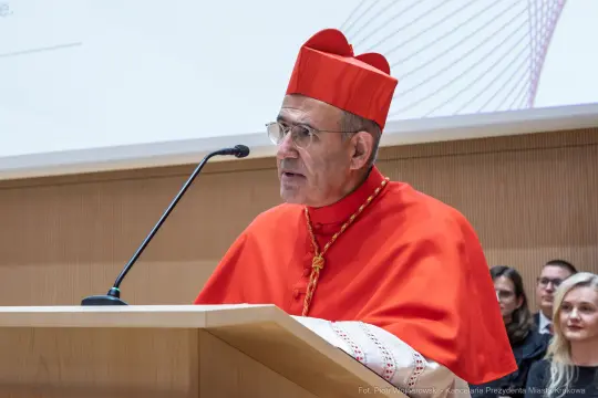 Kardynał w czerwonym stroju wygłasza przemówienie przy mównicy.