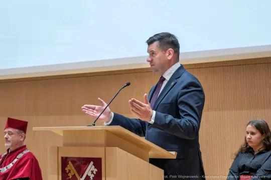 Mężczyzna przemawia przy mównicy, w tle widoczni inni uczestnicy wydarzenia.