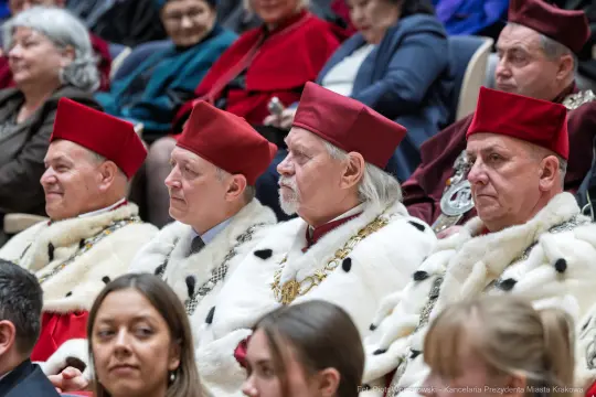 Czterech mężczyzn w czerwonych czapkach i futrzanych płaszczach siedzi na widowni.