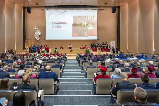 Uroczystość powitania gości w sali konferencyjnej z mówcami i zgromadzonymi uczestnikami.