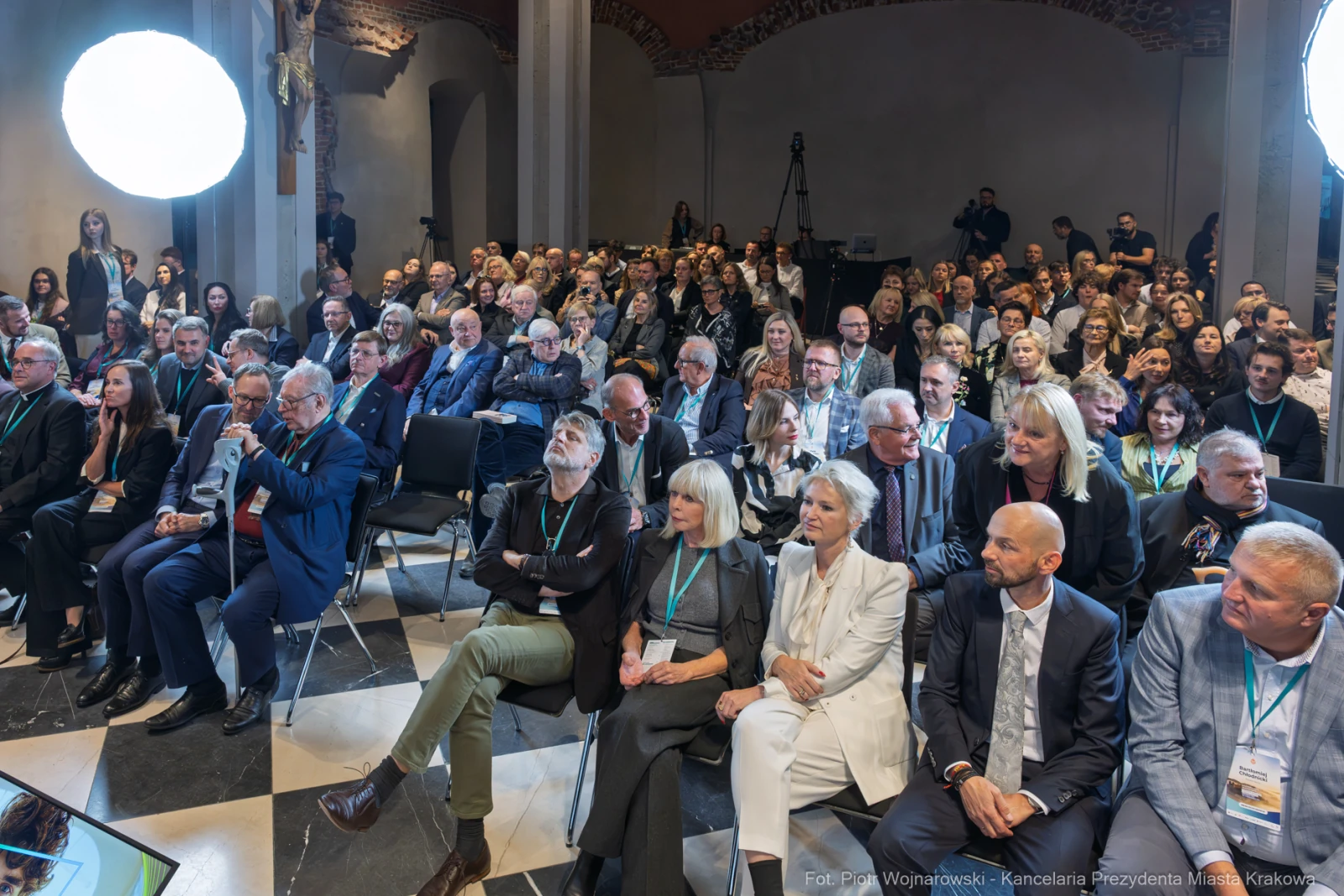 Tłum ludzi siedzących na konferencji, z widocznymi reflektorami i kamerą.  Autor: Piotr Wojnarowski