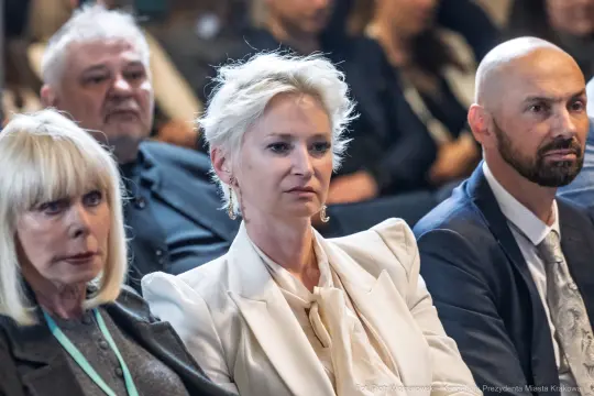 Grupa osób siedzących na wydarzeniu, skupionych na prelekcji.
