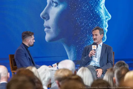 Mężczyzna rozmawia z innym mężczyzną, w tle sylwetka kobiety w stylu futurystycznym.