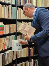 Mężczyzna przegląda książki w bibliotece, trzymając w ręku dwie publikacje.