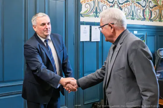 Dwaj mężczyźni podają sobie ręce w eleganckim wnętrzu.