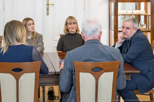 Spotkanie grupy ludzi przy stole w formalnym otoczeniu.