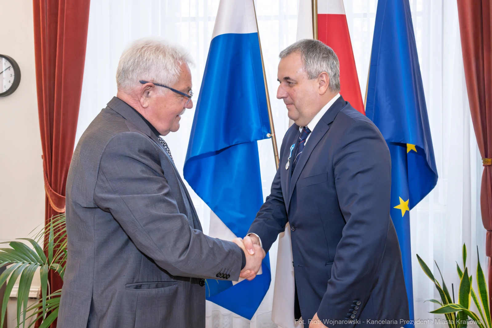 Uścisk dłoni dwóch mężczyzn w garniturach, w tle flagi Polski i Unii Europejskiej.  Autor: Piotr Wojnarowski