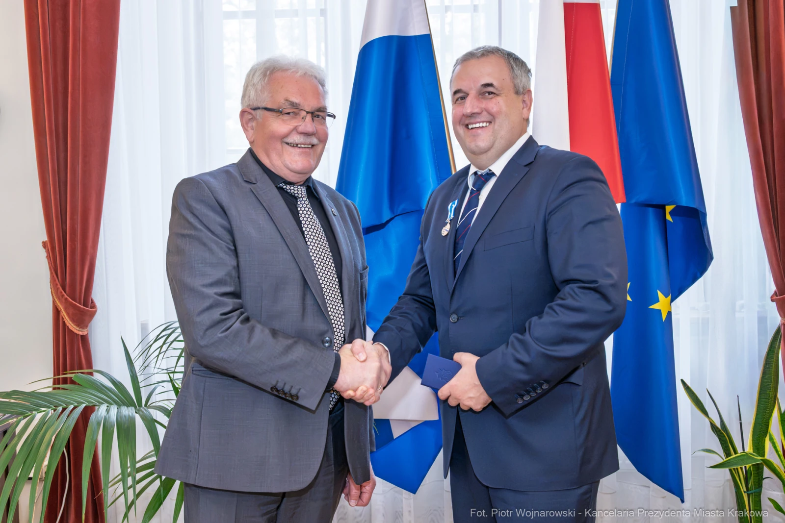 Dwaj mężczyźni uścisnęli sobie dłonie, w tle flagi Polski i Unii Europejskiej.  Autor: Piotr Wojnarowski