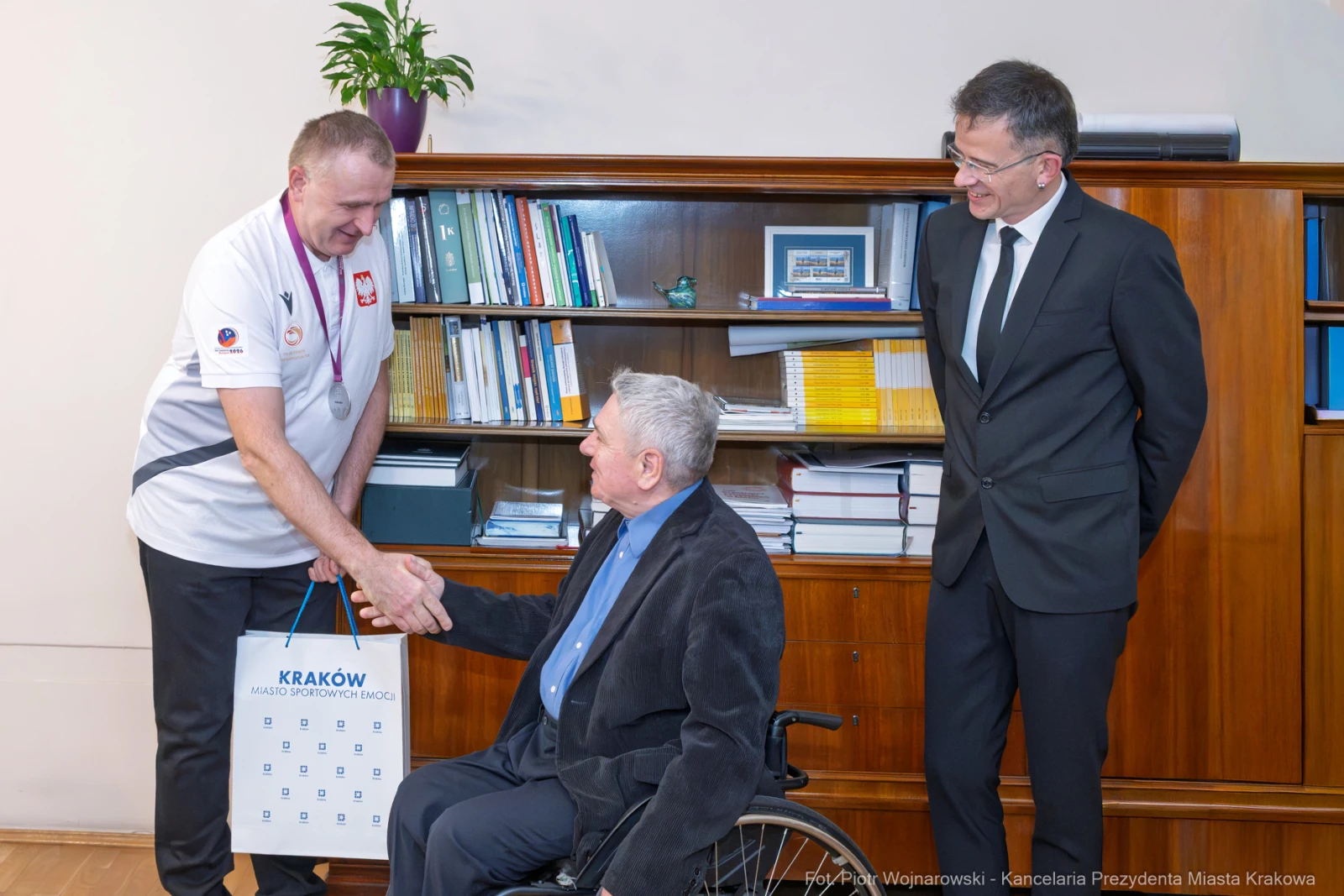 Spotkanie dwóch mężczyzn, jeden w wózku inwalidzkim, wręczenie upominku.  Autor: Piotr Wojnarowski