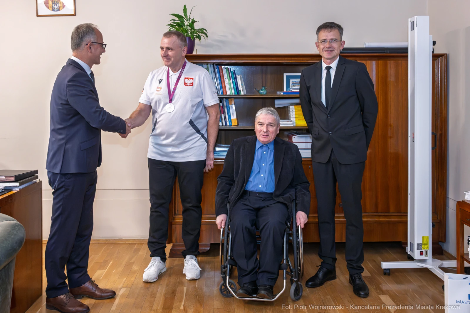 Spotkanie z medalistą, wręczenie medalu, obecność dwóch mężczyzn w garniturach oraz osoby na wózku.  Autor: Piotr Wojnarowski