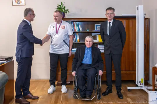 Spotkanie z medalistą, wręczenie medalu, obecność dwóch mężczyzn w garniturach oraz osoby na wózku.