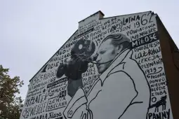 Mural z postacią trzymającą kamerę, otoczony tekstem i datami.