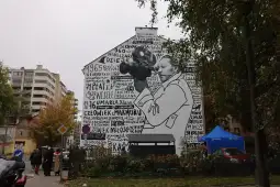 Mural z postacią trzymającą aparat fotograficzny, otoczony tekstami i datami.