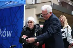 Starsza kobieta z mikrofonem rozmawia z mężczyzną w garniturze, obok stoi kobieta w jasnej bluzie.