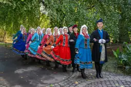 Grupa osób w tradycyjnych strojach ludowych tańczących w parku.