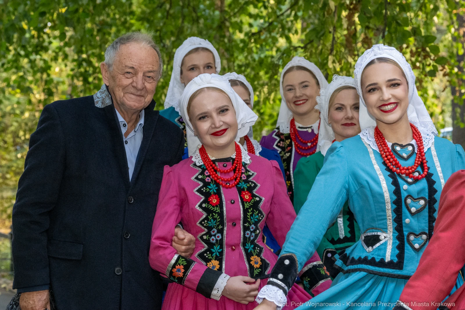 Mężczyzna w eleganckim ubraniu z grupą kobiet w tradycyjnych strojach ludowych.  Autor: Piotr Wojnarowski