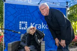 Kobieta w okularach przeciwsłonecznych rozmawia z mężczyzną w garniturze pod namiotem z logo Krakowa.