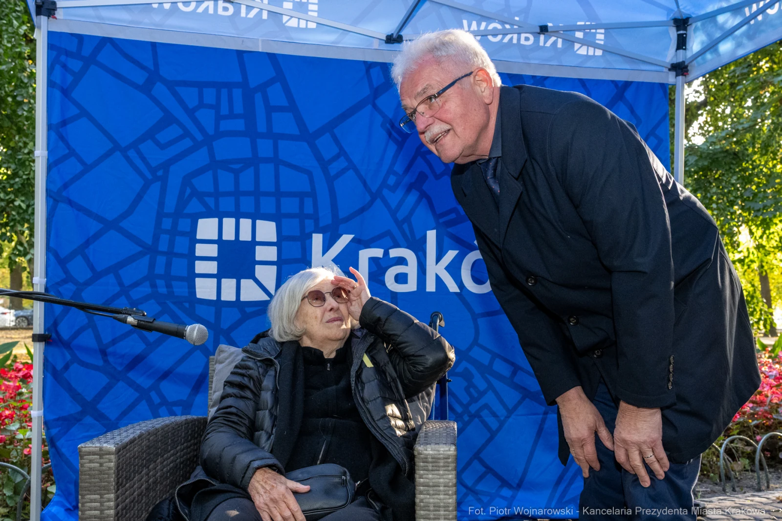 Kobieta w okularach przeciwsłonecznych rozmawia z mężczyzną w garniturze pod namiotem z logo Krakowa.  Autor: Piotr Wojnarowski